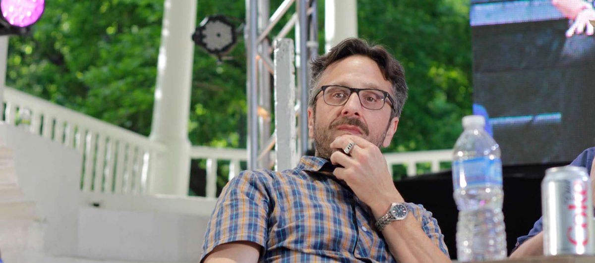 Marc Maron in glasses and a plaid shirt, resting his chin on his hand at an outdoor event