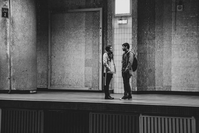 Two people in a busy train station, one carrying luggage, a hint of drama and movement