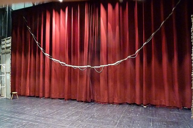 A red theatre curtain hanging across a stage with a white rope looped along it