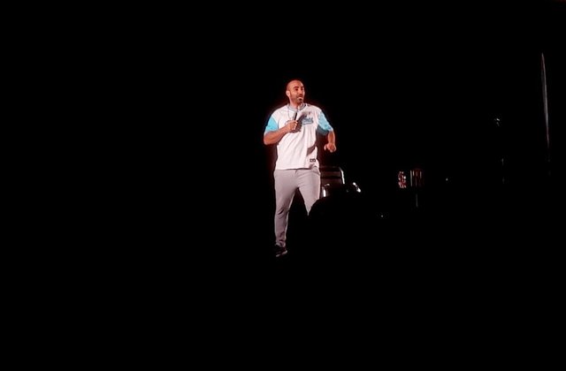 Comedian Yohay Sponder performing on a dark stage with a microphone in hand
