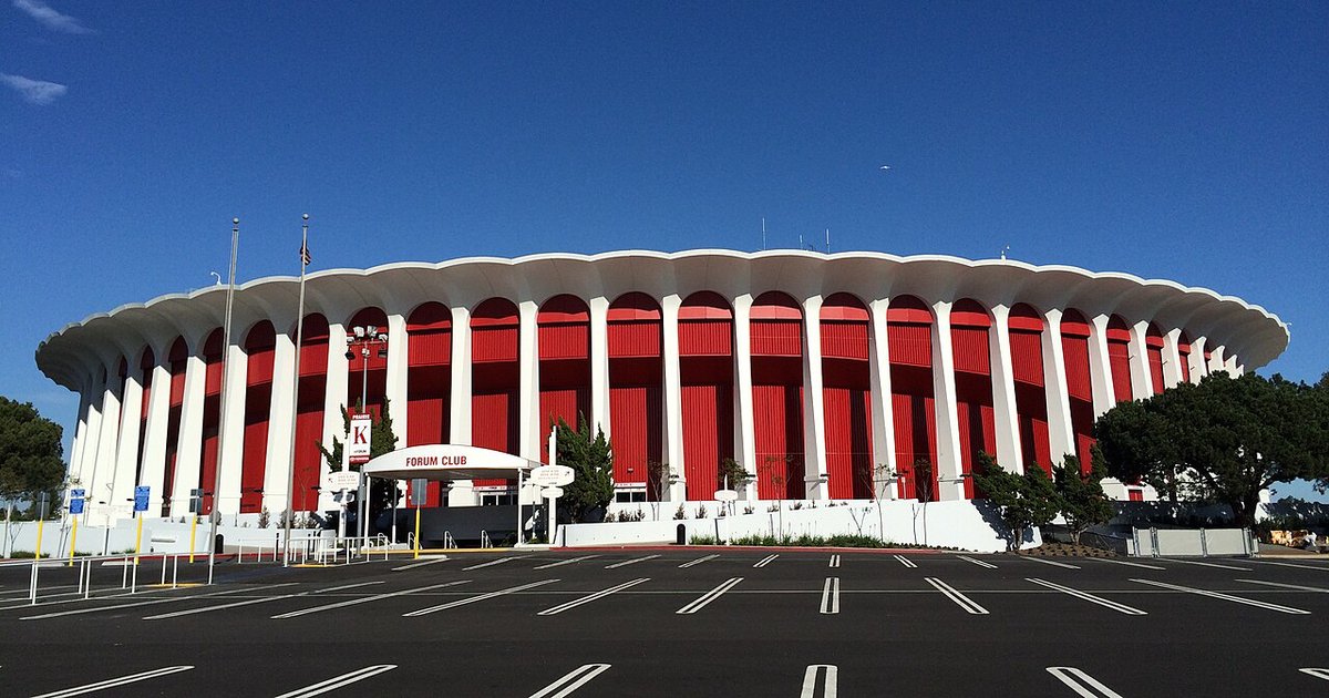 Front of the Kia Forum arena in Inglewood, white columns and red panels under a blue sky