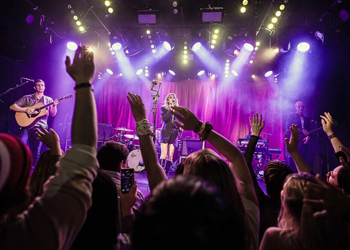Fans with raised hands in front of the Teragram Ballroom stage under purple and white lights