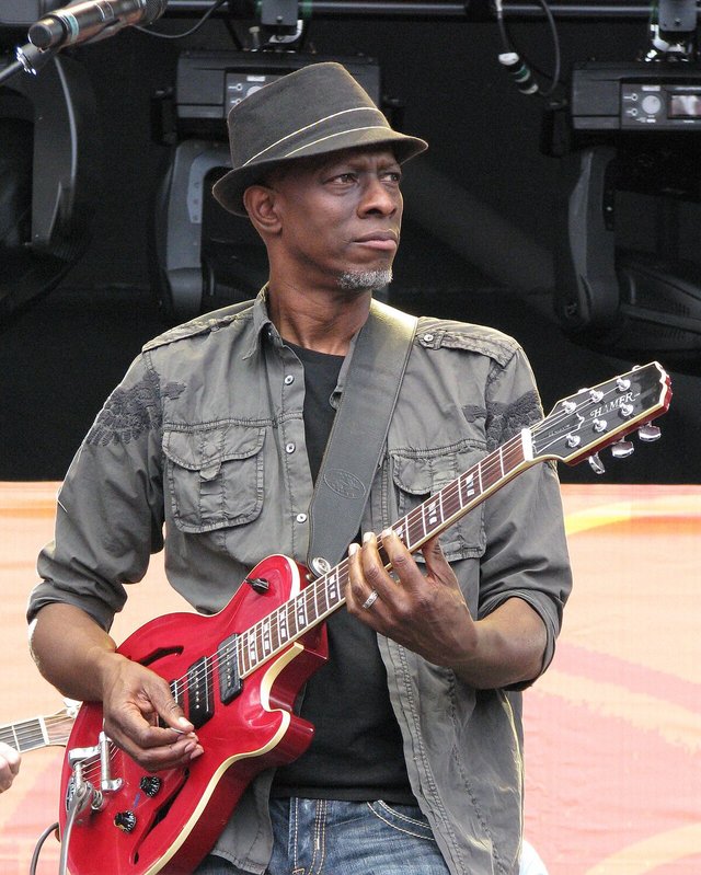 Keb' Mo' in a brimmed hat playing a red semi-hollow guitar on an outdoor stage