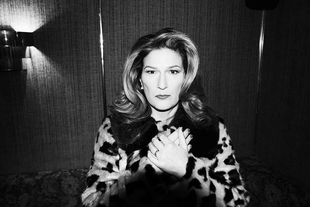 Black and white portrait of Ana Gasteyer in a leopard print coat, hands crossed over her chest
