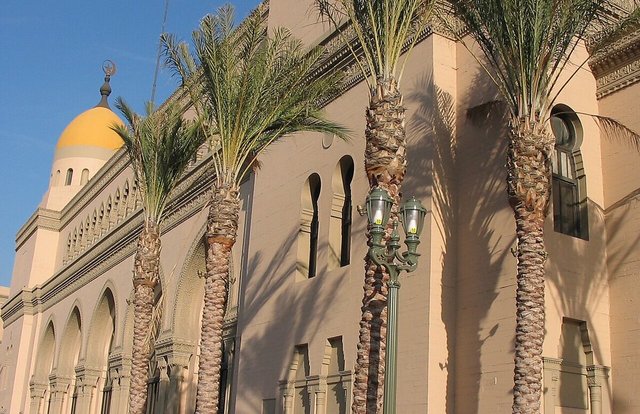 Sunlit Shrine Auditorium facade with a gold dome and palm trees, next to the Shrine Expo Hall complex