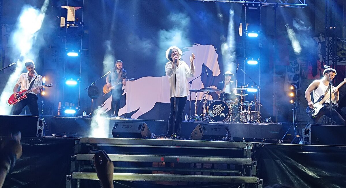 Arde Bogota performing on a smoky, blue-lit stage with a singer at center, two guitarists, a bassist and a drummer