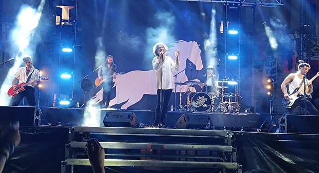 Arde Bogota performing on a smoky, blue-lit stage with a singer at center, two guitarists, a bassist and a drummer