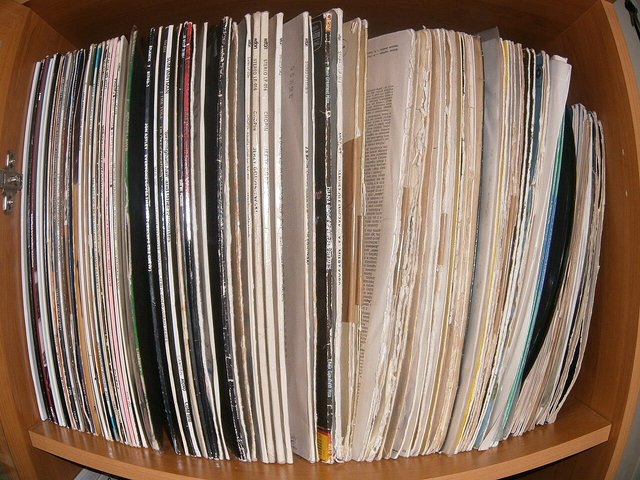 A wooden cubby shelf filled with vinyl records standing on edge