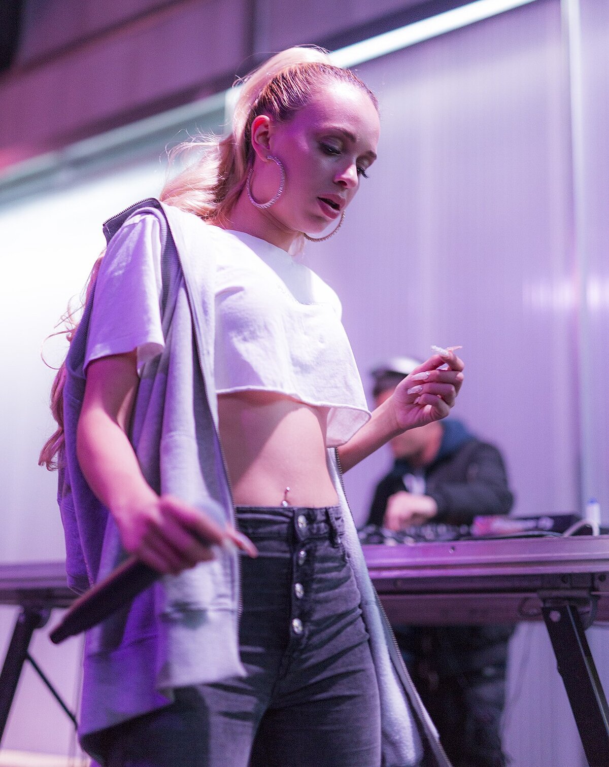 Bad Gyal performing on stage in a white crop top with a DJ behind her under purple light