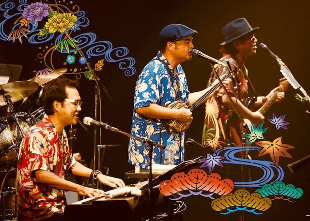 Three members of a band performing on stage with a keyboard, a sanshin and a guitar, framed by Japanese wave and maple leaf artwork