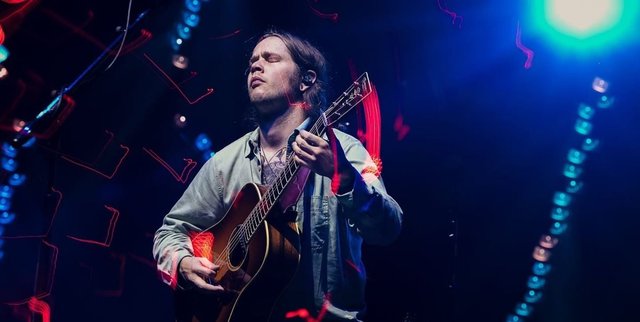 Billy Strings playing an acoustic guitar onstage under blue and red concert lights