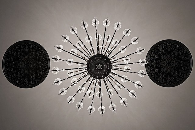 A circular starburst light fitting on a plain ceiling between two black round panels