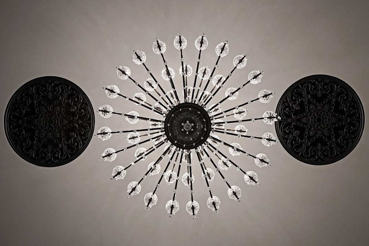 A circular starburst light fitting on a plain ceiling between two black round panels
