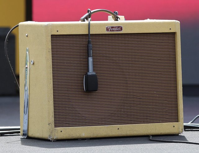 A cream-colored guitar amplifier with a microphone clipped in front of the speaker, against a pink backdrop