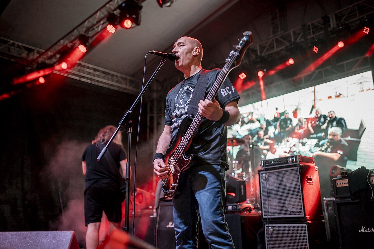 A bassist and band on a stage with red lights and a video screen