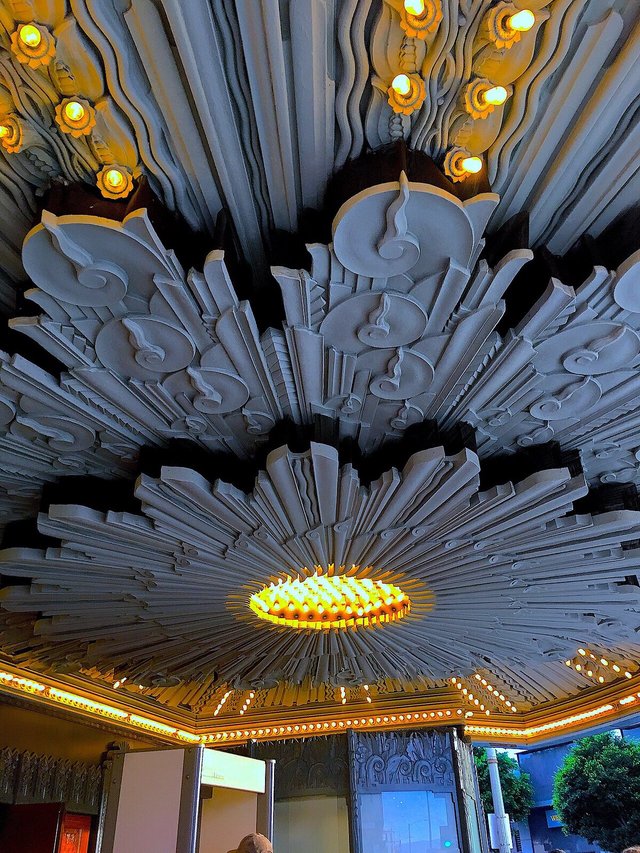 Sunburst Art Deco ceiling of a theater entrance lit by rows of yellow bulbs