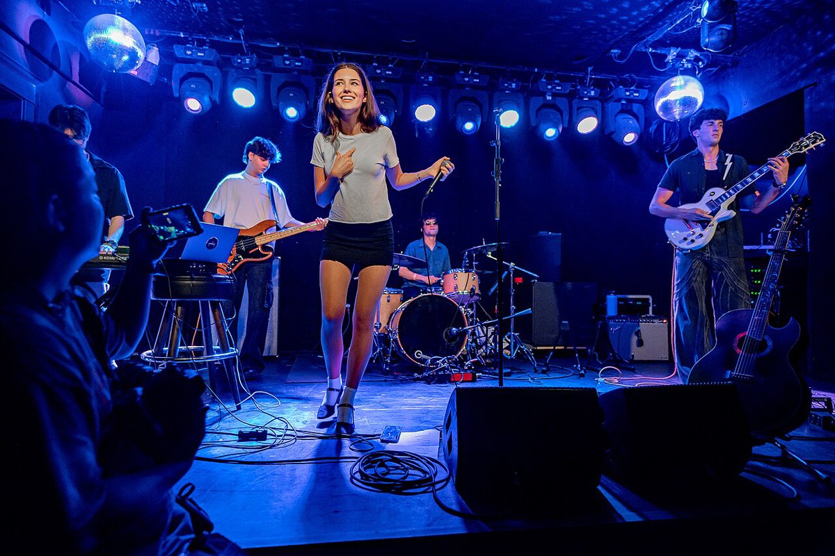 A band on a small club stage lit in blue, with the audience's heads in the foreground