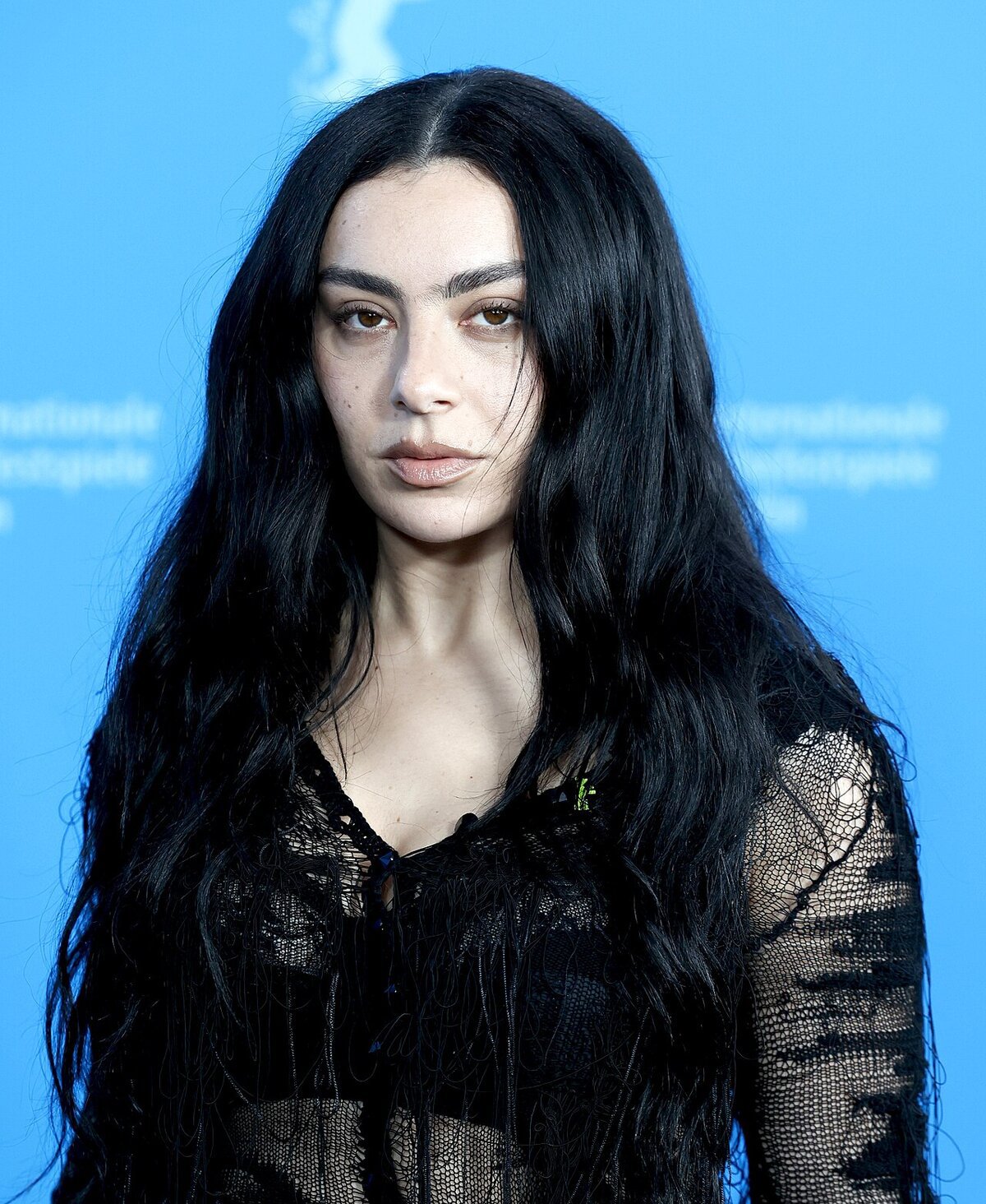 Portrait of Charli xcx with long black hair against a blue backdrop