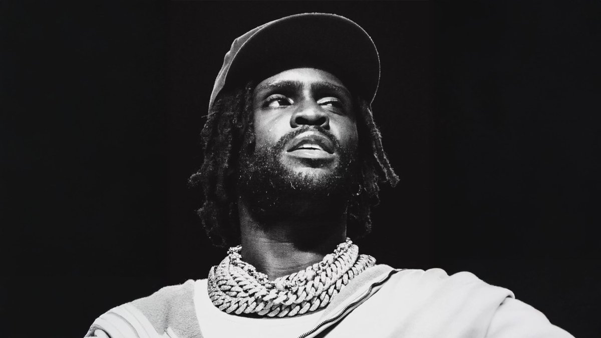 Black and white photo of Chief Keef in a ball cap and stacked chain necklaces, looking up from the stage