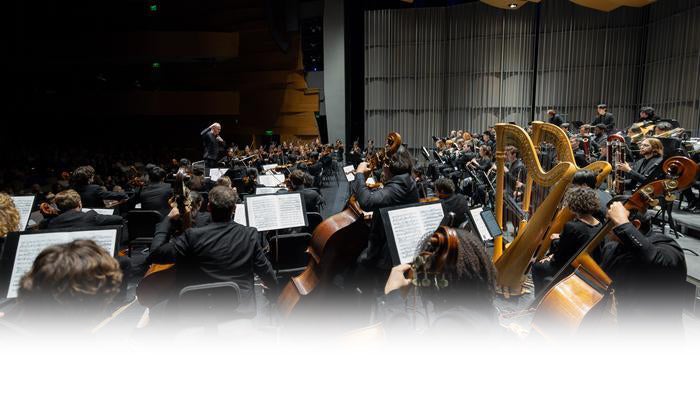 Colburn Orchestra musicians with harps, cellos and violins on stage at The Soraya as the conductor leads from the podium