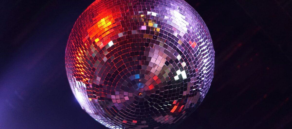 Mirrored disco ball lit in red and purple against a dark ceiling