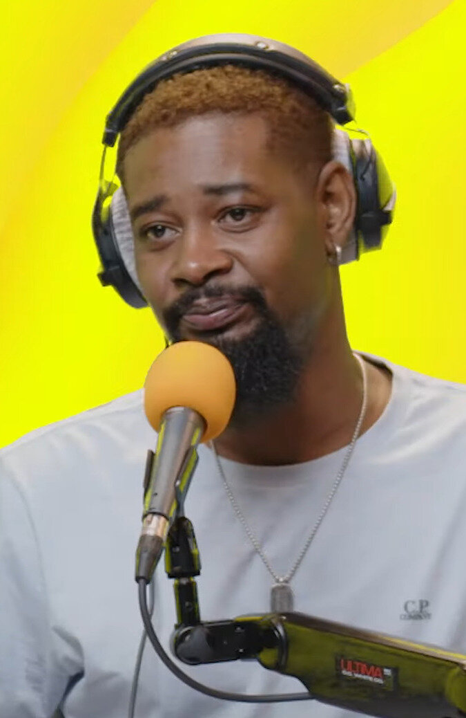 Danny Brown wearing headphones and speaking into a microphone against a yellow background