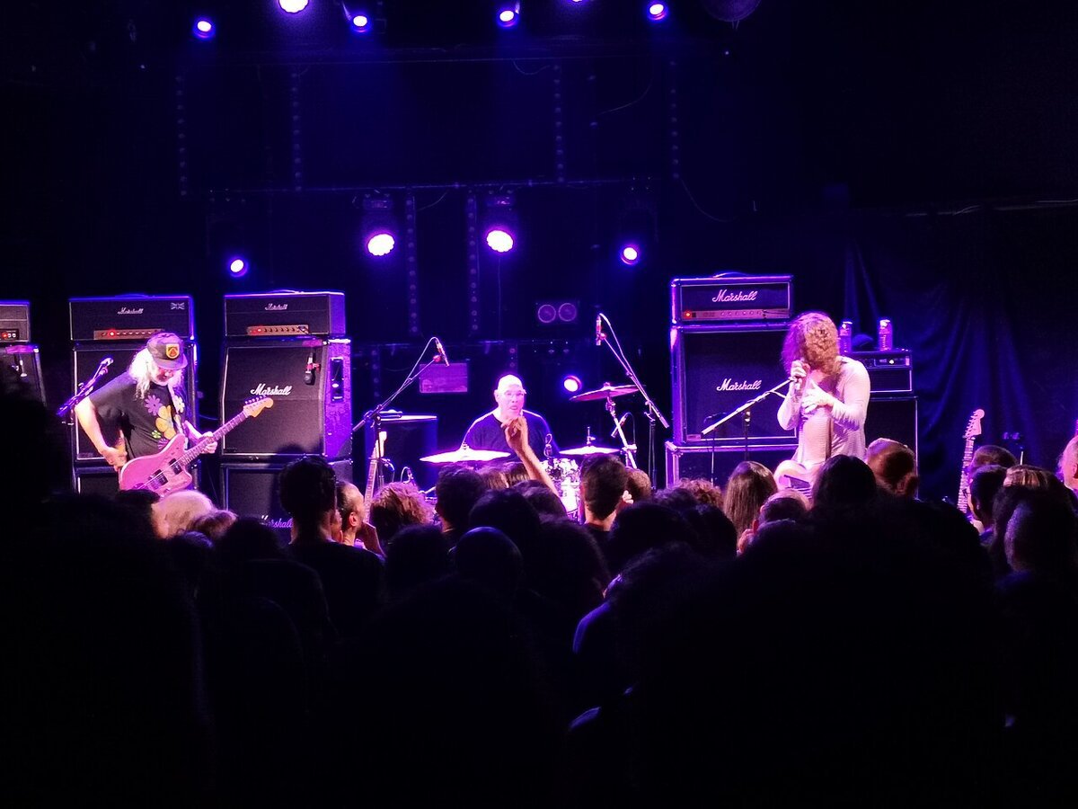 Dinosaur Jr. performing on a purple-lit stage in front of Marshall amplifier stacks and a crowd