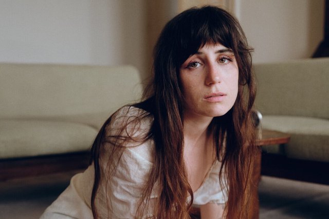 Portrait of a woman with long dark hair and bangs seated in a softly lit living room