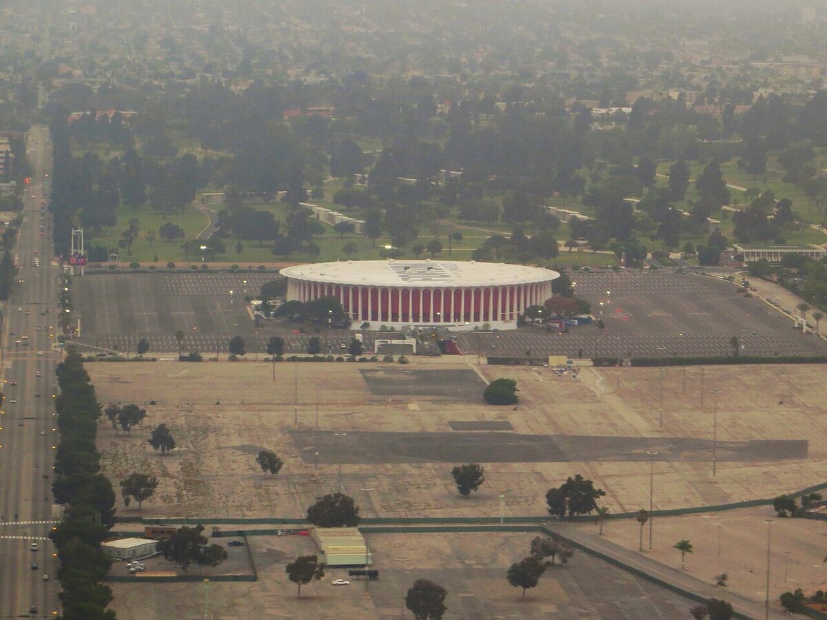 Aerial view of the round Kia Forum arena surrounded by parking lots in Inglewood