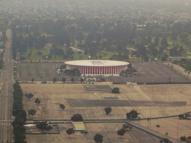 Aerial view of the round Kia Forum arena surrounded by parking lots in Inglewood