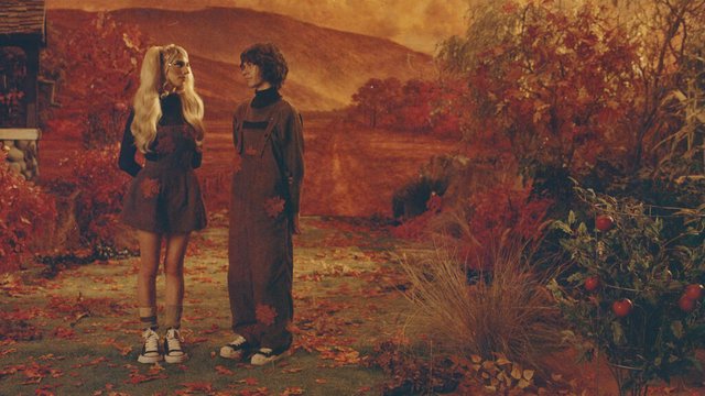 DOMi and JD Beck standing in overalls in an autumn garden of red leaves and tomato plants, the promo image for the Who Asked? Tour