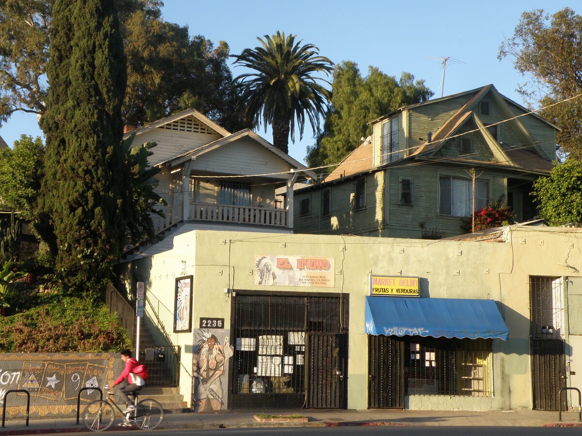 Sunset Boulevard in Echo Park with a cyclist passing old wooden houses above a small corner market