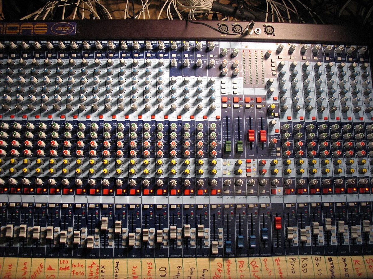 Close-up of a large analog mixing console with rows of faders, knobs and channel strips
