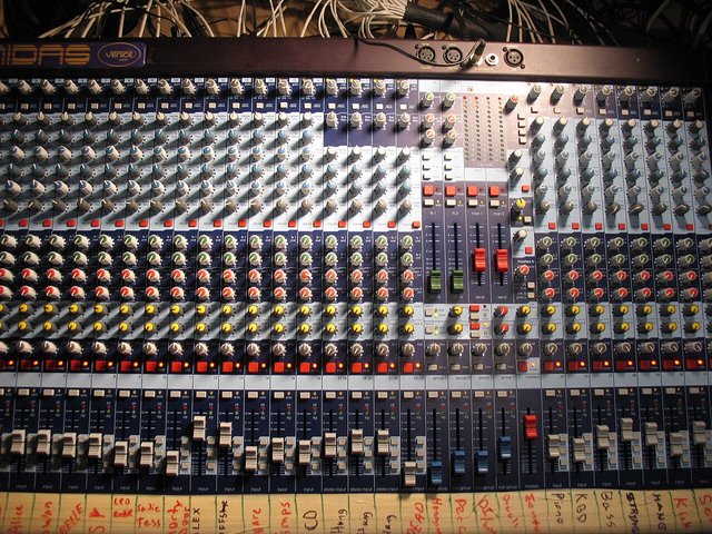 Close-up of a large analog mixing console with rows of faders, knobs and channel strips