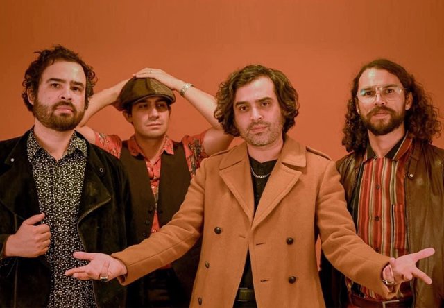 Four members of the band Enjambre posed in front of an orange wall