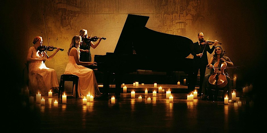 String players and a pianist performing around a grand piano surrounded by candles
