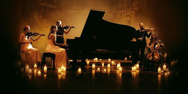 String players and a pianist performing around a grand piano surrounded by candles