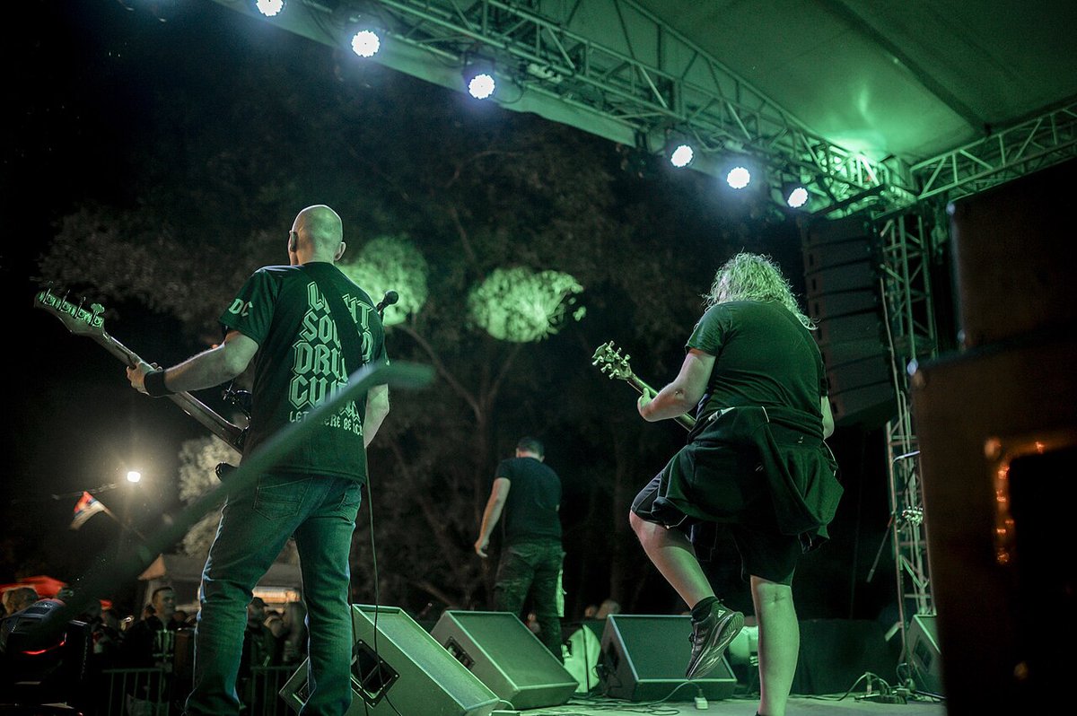 A band performing on an outdoor stage under green stage lights