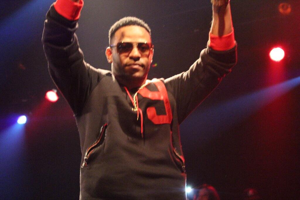 Eric Bellinger performing on stage under red and blue lights with both arms raised
