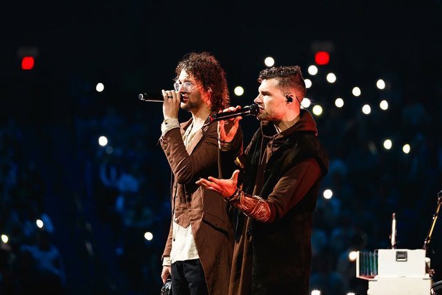 Joel and Luke Smallbone of For King and Country singing into microphones on stage in front of a crowd lit by phone lights