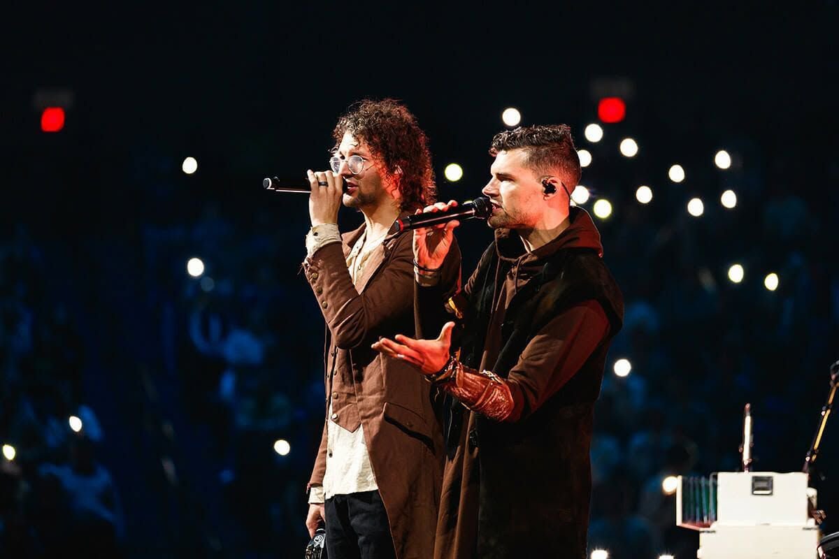 Joel and Luke Smallbone of For King and Country singing into microphones on stage in front of a crowd lit by phone lights
