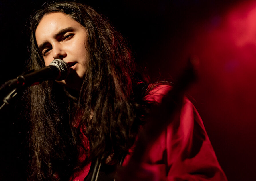 Singer with long dark hair at a microphone, lit in red stage light