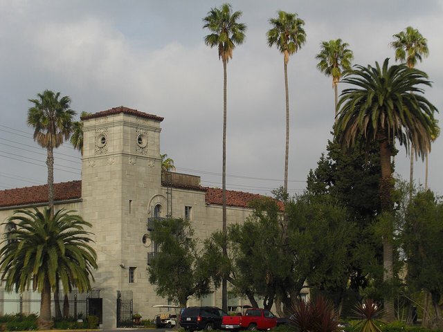 The Spanish-style main building of Hollywood Forever Cemetery with tall palm trees under a cloudy sky