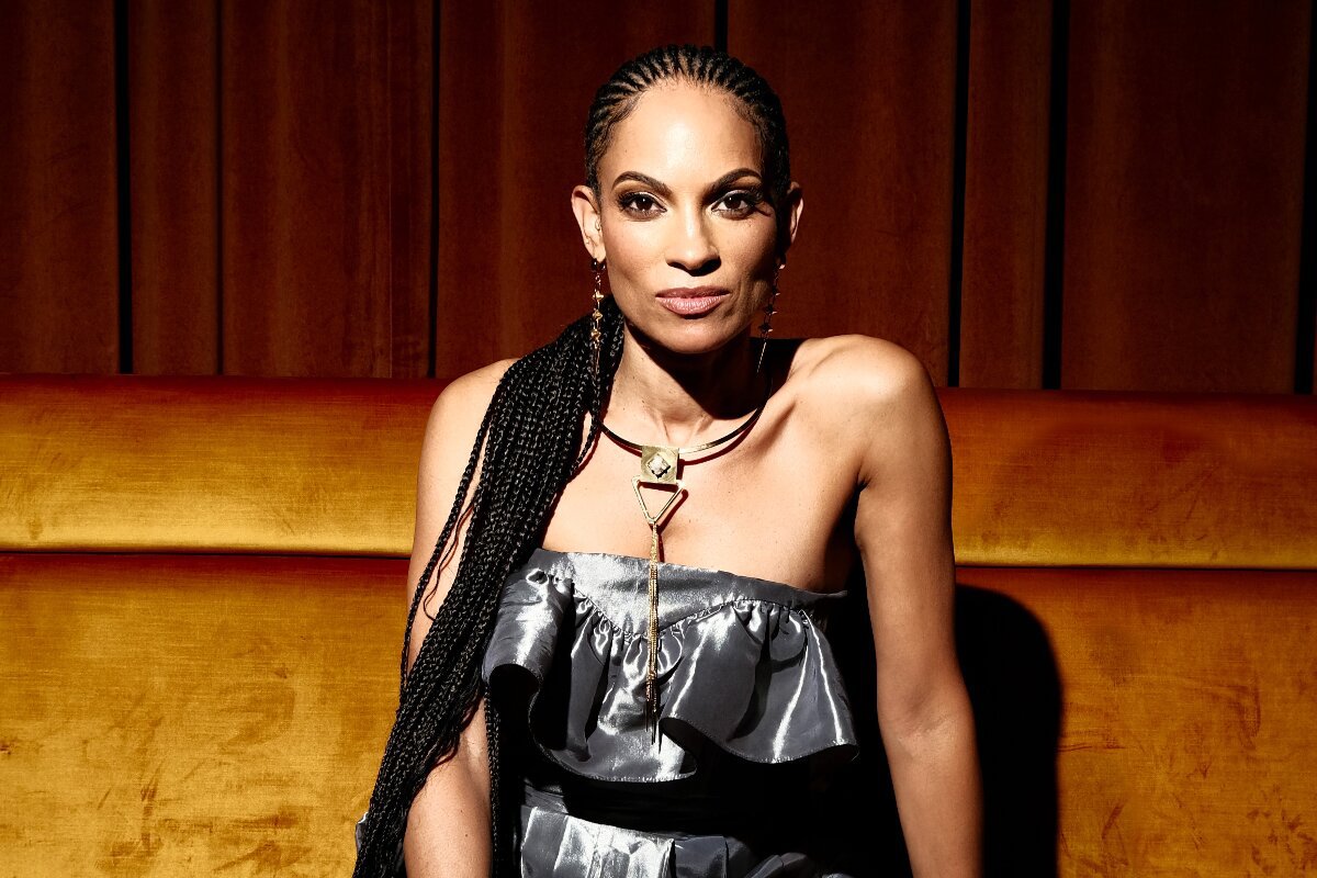 Goapele seated on an amber velvet banquette in a silver ruffled top