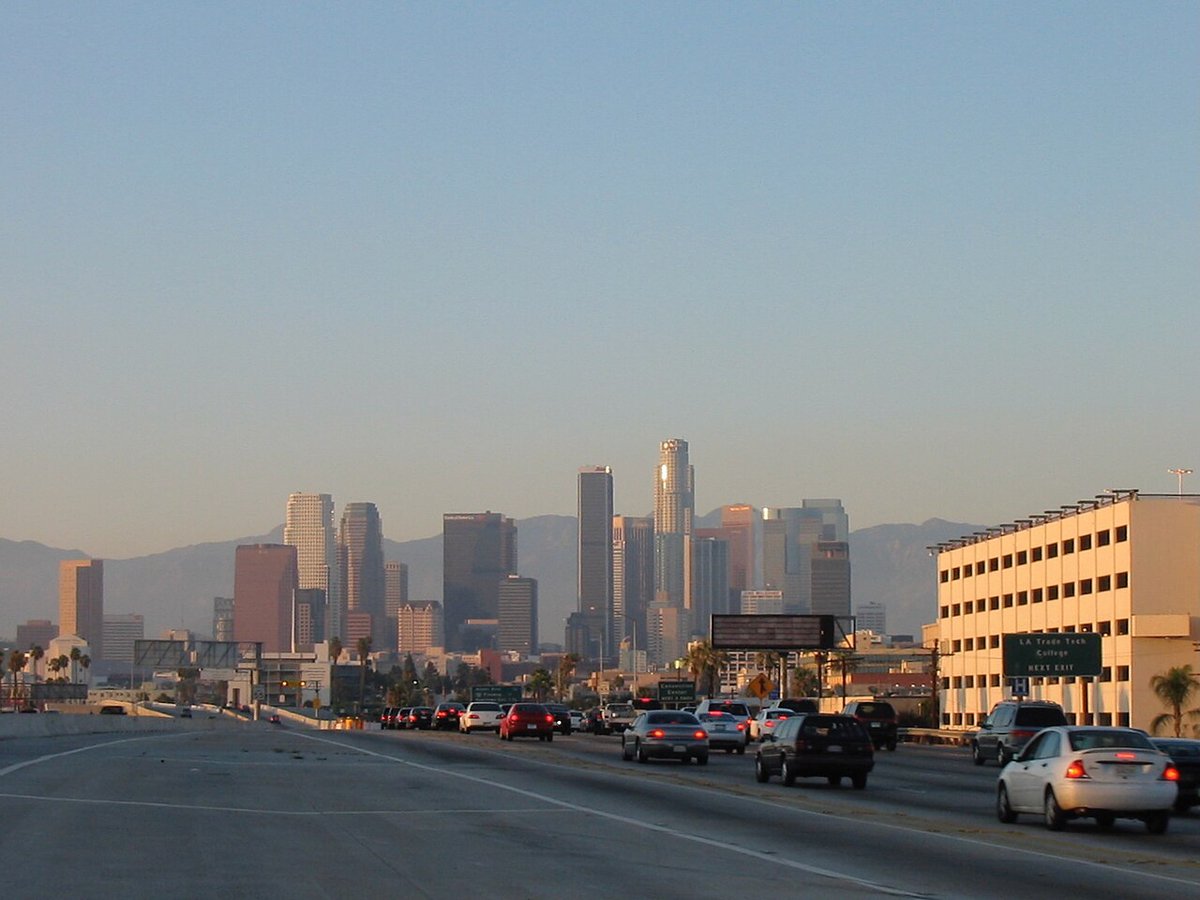 Downtown Los Angeles skyline at dusk seen from a busy freeway with mountains behind