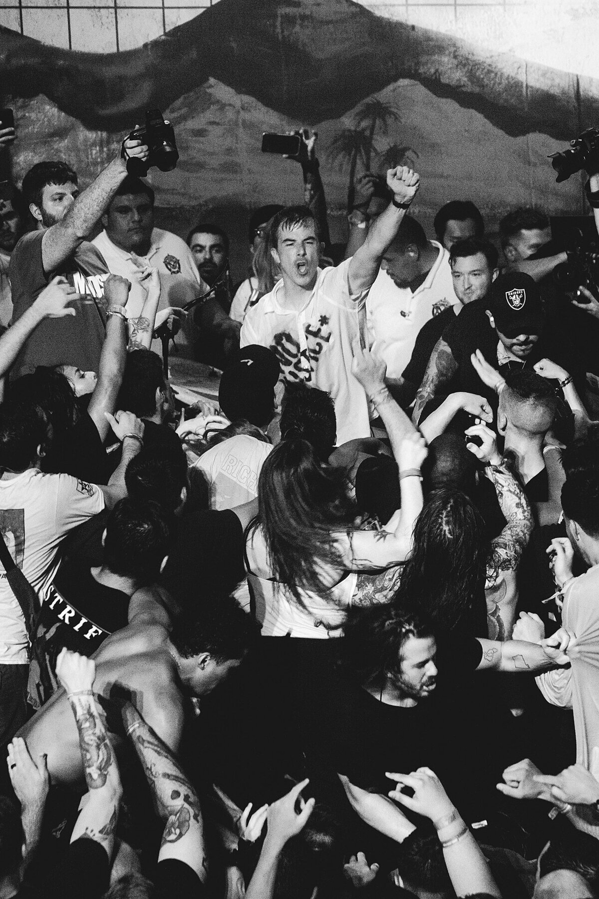 Black and white shot of a packed hardcore show, a singer with a raised fist surrounded by fans and photographers