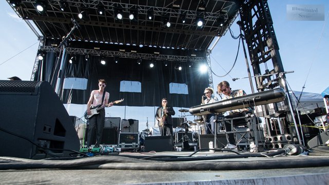 Houndmouth's four band members playing on an outdoor festival stage under stage lights