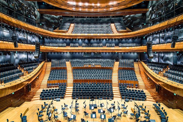 An empty modern concert hall with tiered blue seating rising around a wooden stage