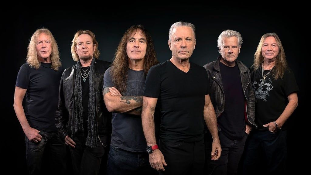 The six members of Iron Maiden posing in black t-shirts and leather jackets against a dark backdrop