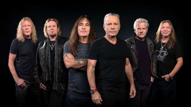 The six members of Iron Maiden posing in black t-shirts and leather jackets against a dark backdrop